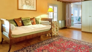 Ein gemütliches Zimmer mit Holzbalkendecke, einem Bett mit grün-braunen Kissen, einem gerahmten Bild an der Wand und einem roten Teppich mit Muster.