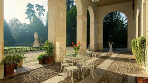 Eine Terrasse im Freien mit Steinboden, weißen Metallstühlen und einem Tisch mit einem Blumenstrauß.