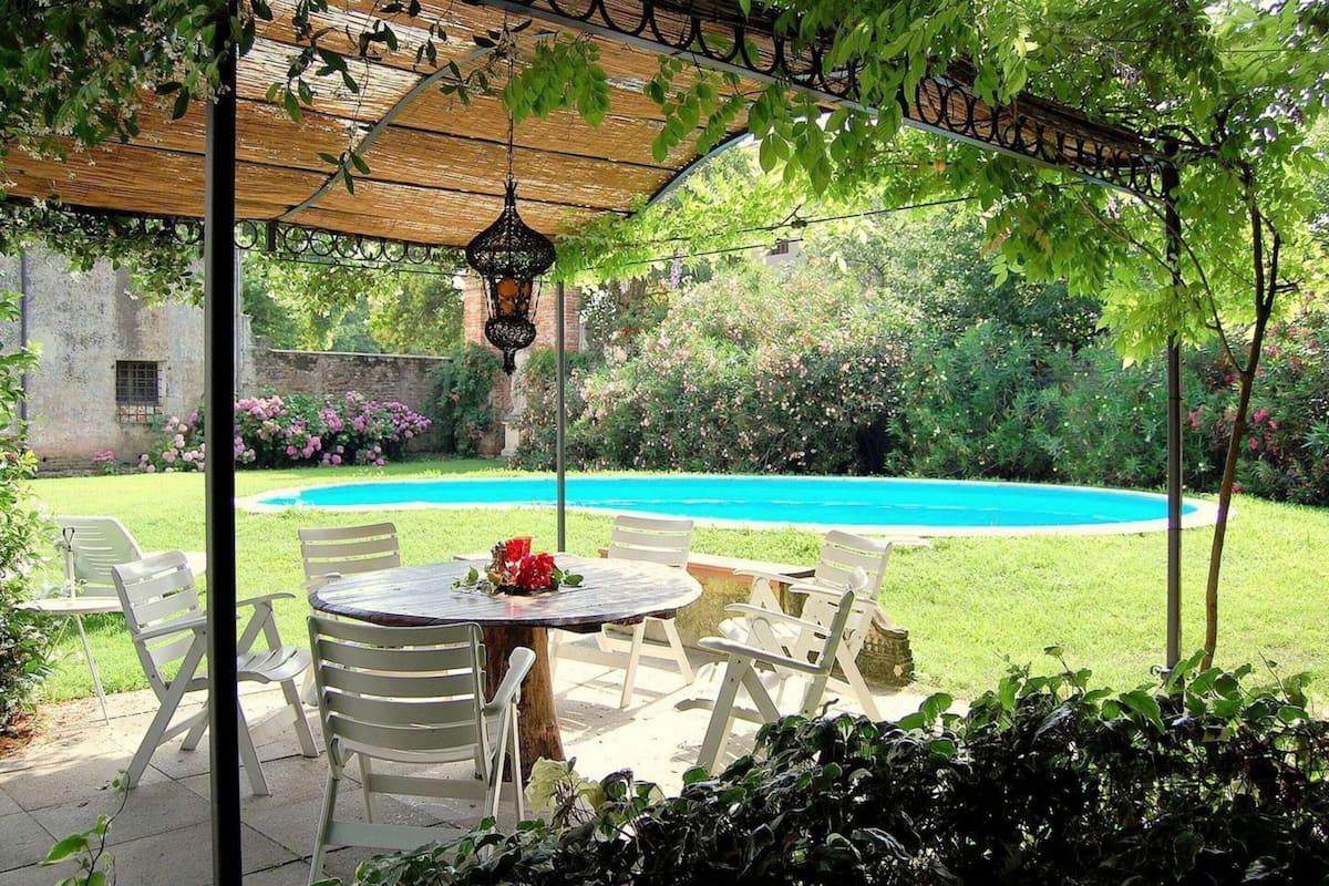 Eine Terrasse im Freien mit einem runden Tisch und Stühlen, einer hängenden Laterne und einem Pool im Hintergrund.