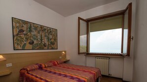 A bedroom with a bed, a large window, a radiator, and a wall-mounted painting. - Belvilla by OYO Gianni C Cinque Piao Due (Torri del Benaco)