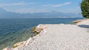 A pebble beach with clear water and distant mountains. - Belvilla by OYO Gianni C Cinque Piao Due (Torri del Benaco)