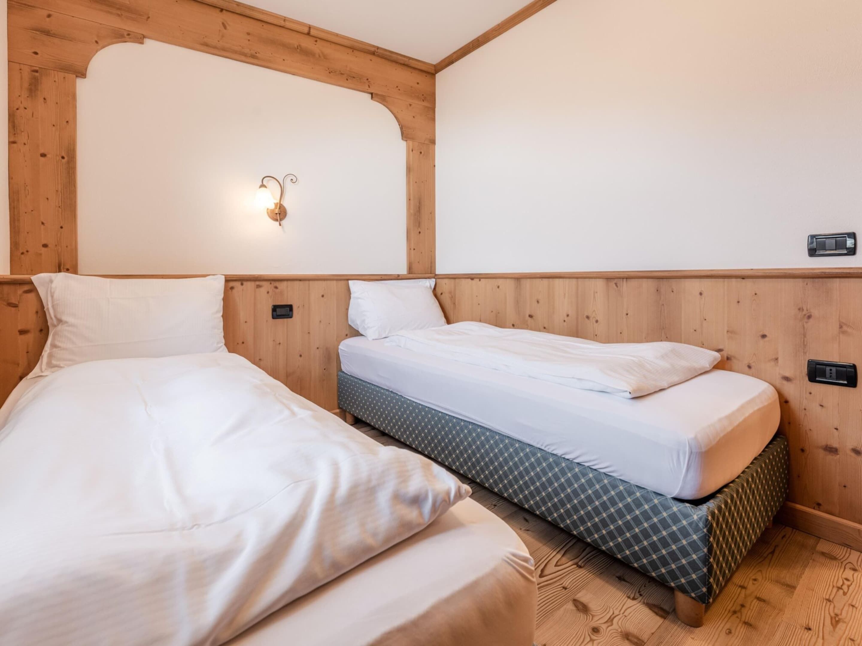 Una habitación con dos camas, paneles de madera, una lámpara fijada a la pared y un enchufe.