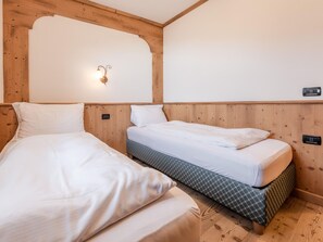 A room with two beds, wooden paneling, a wall-mounted light fixture, and a power outlet. - Belvilla by OYO Maso Margherita Quadrilocale (Commezzadura)