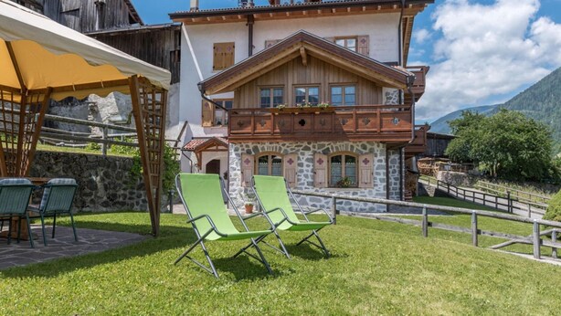 A chalet with a stone facade, wooden balcony, and two green lawn chairs in the foreground. - Belvilla by OYO Maso Margherita Quadrilocale (Commezzadura)