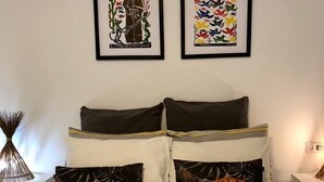 A neatly made bed with two pillows, a heart-shaped towel arrangement, and tropical-themed pillows. - Pousada das Oliveiras (Ipojuca)