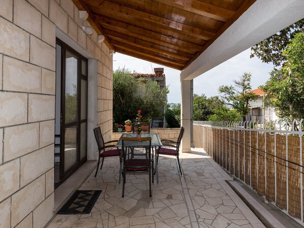 A covered outdoor seating area with a table and chairs, a stone wall, and a view of the surrounding neighborhood.