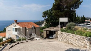 Ein Küstengebäude mit rotem Ziegeldach, einer Treppe, die zu einer Tür führt, und Blick aufs Meer.
