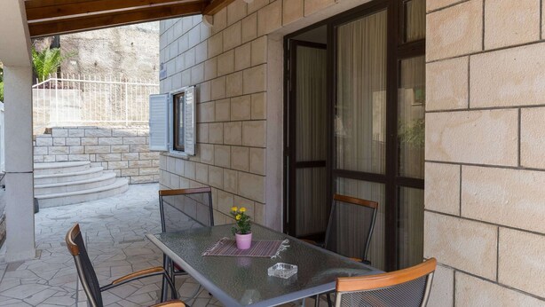 Eine Terrasse im Freien mit Tisch und Stühlen, einem Blumentopf und Blick auf eine steinerne Treppe, die zu einer Tür führt.