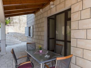Una terrazza esterna con tavolo e sedie, una pianta in vaso e vista su una scala in pietra che conduce a una porta.