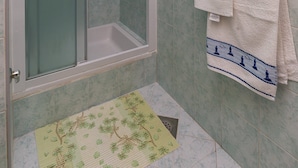 Eine Dusche mit Glastür, ein Handtuchhalter mit zwei Handtüchern und eine grüne Matte am Boden.
