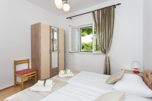A bedroom with a bed, a chair, a wardrobe, a window with curtains, and a bedside lamp.