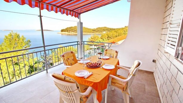 Un balcon avec une table dressée pour le dîner, offrant une vue sur une étendue d’eau et sur la verdure.