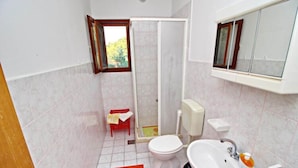 Une salle de bain avec des toilettes, un lavabo, une douche et une petite fenêtre.