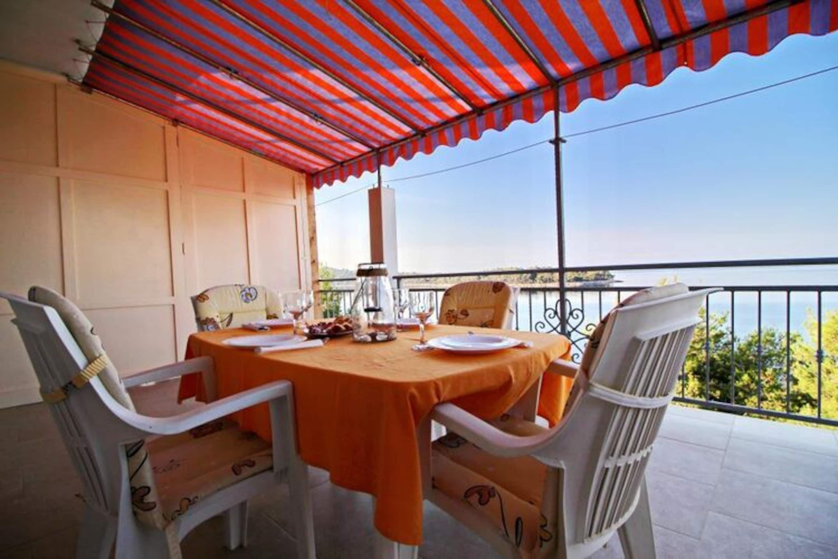 Un espace repas avec une table et des chaises, un auvent à rayures et une vue sur la mer.