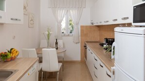 Et moderne køkken med hvide skabe, et spisebord med stole, et køleskab og en mikrobølgeovn.