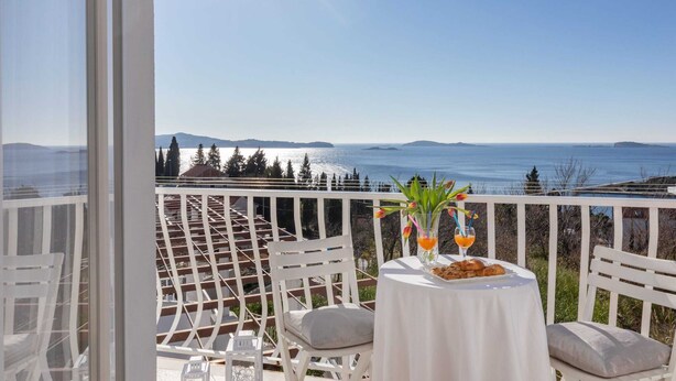 En balkon med et bord dækket til to, der kigger ud over et smukt havlandskab og fjerne øer.