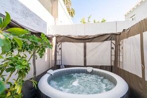 Ein Whirlpool in einem überdachten Außenbereich mit einer weißen Wand und einer Pflanze in der Nähe.