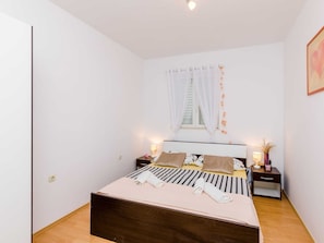 A bedroom with a bed, two bedside tables, a window with curtains, and a wall-mounted light fixture. - Apartment Antej - One Bedroom Apartment With Terrace and City View (Dubrovnik)