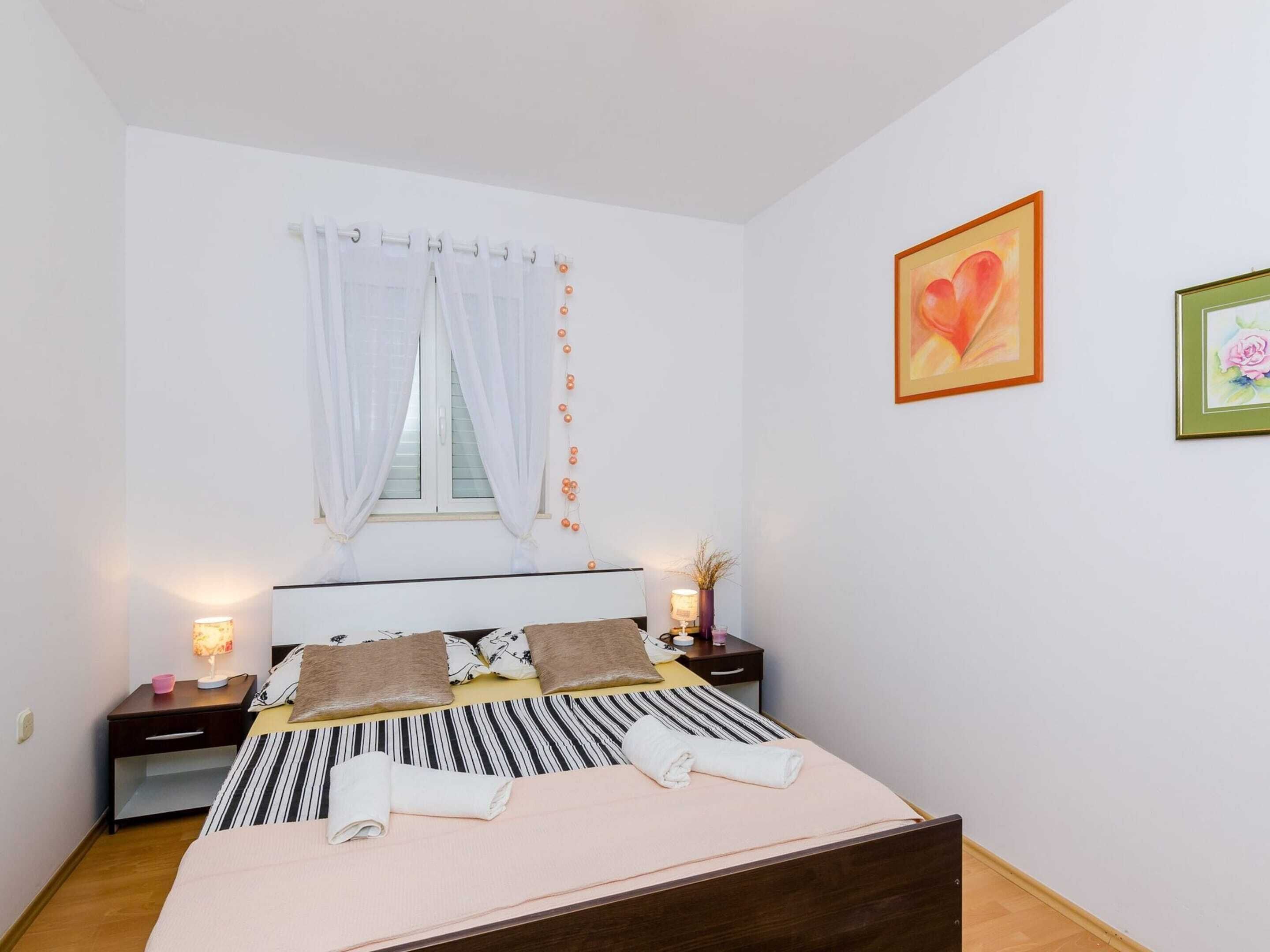 A bedroom with a bed, a window with curtains, bedside tables with lamps, and two framed pictures on the wall.