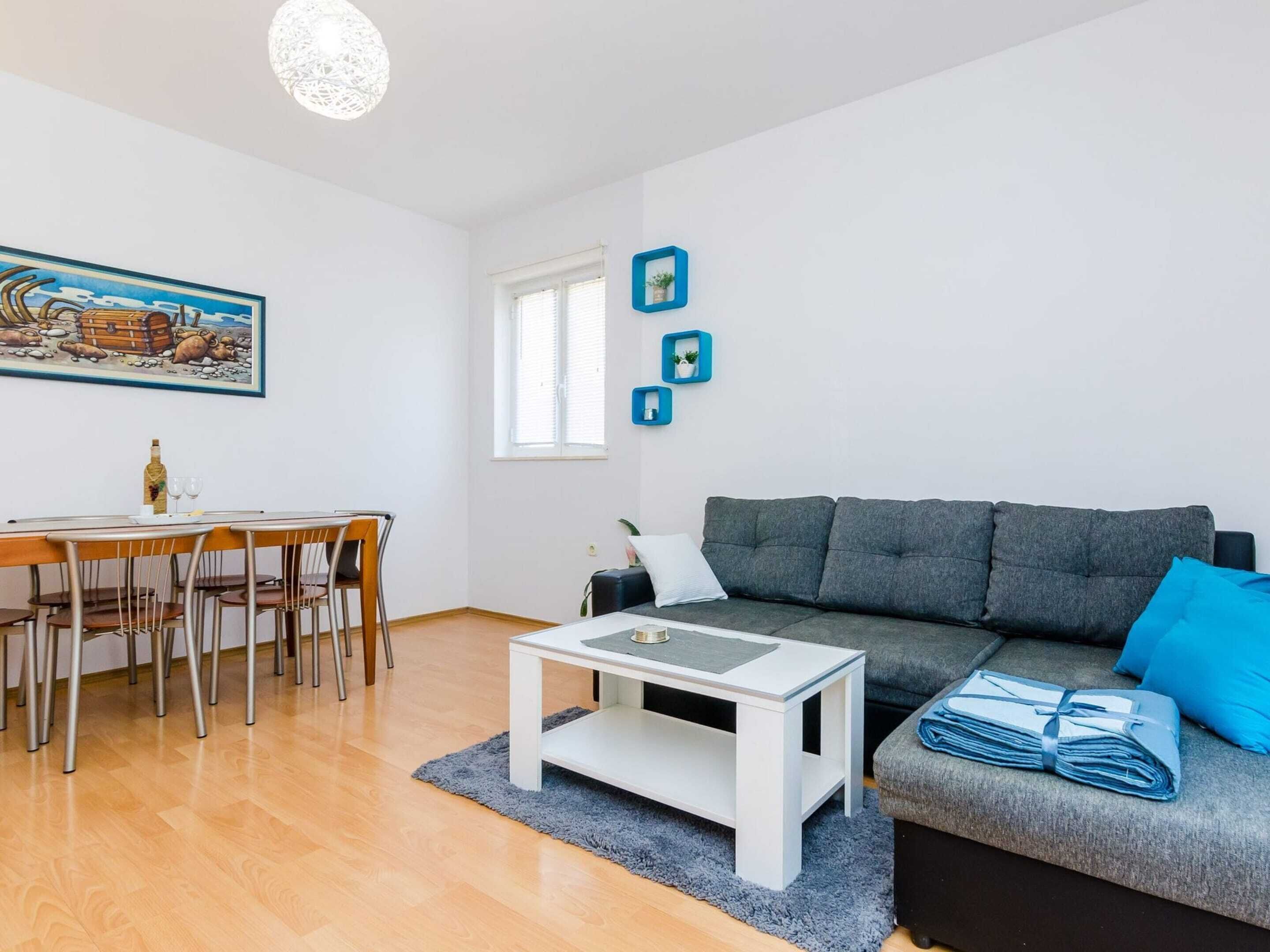 A modern living room with a grey sofa, a white coffee table, a dining table with chairs, and a painting on the wall.