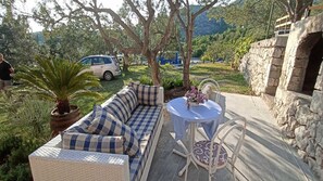 An outdoor seating area with a sofa and a table, surrounded by greenery and a stone wall.