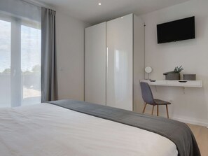A modern bedroom with a bed, a desk, a chair, a TV, and a wardrobe.