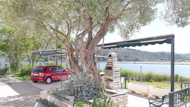 Un área de estacionamiento con un coche rojo, un banco de piedra y un pabellón con vistas a un lago.