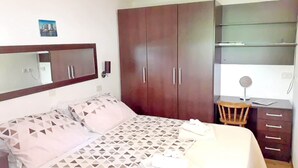 Un dormitorio con cama, armario, escritorio con silla y espejo.