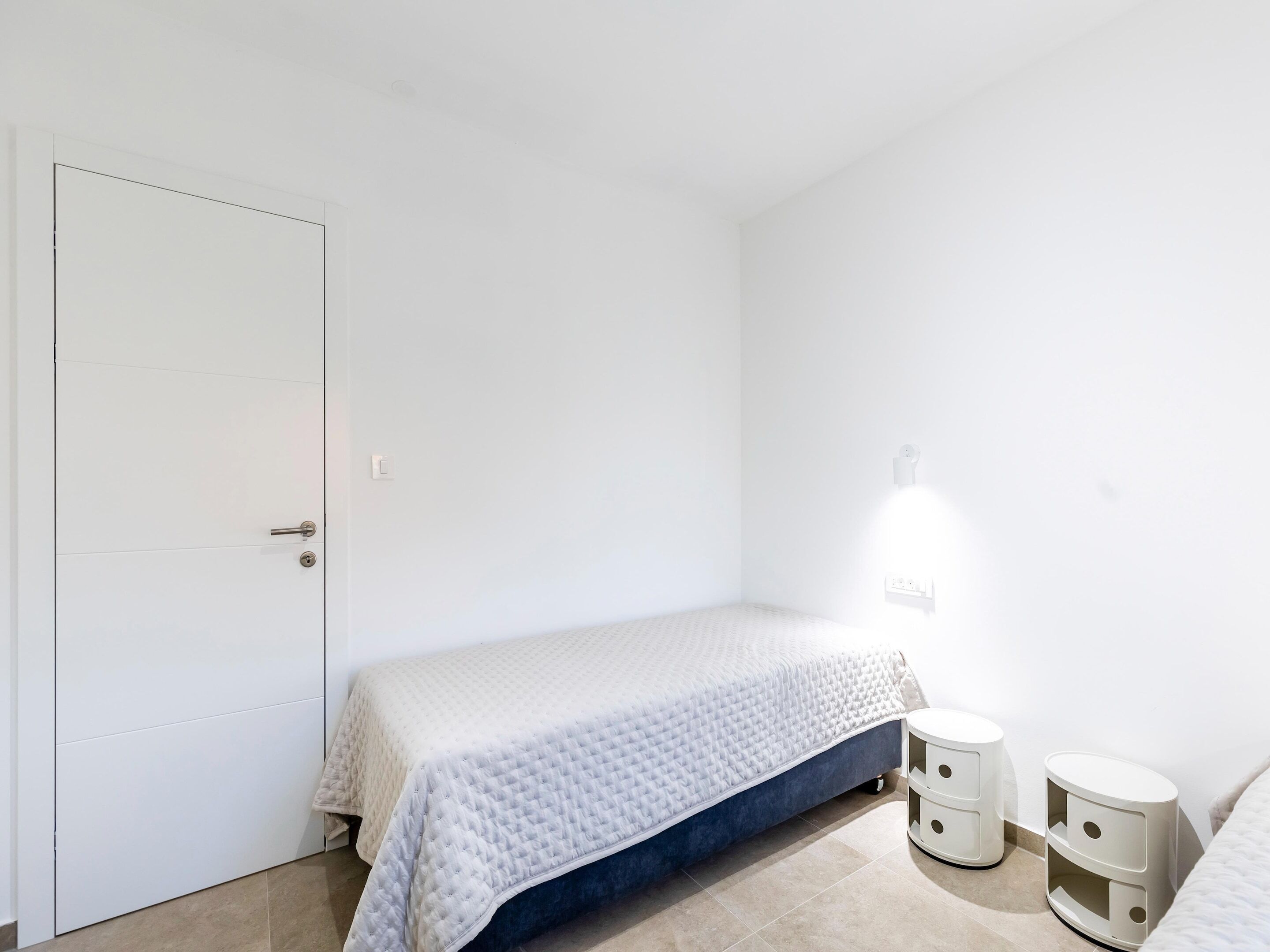 Un dormitorio con una cama, una puerta y dos mesitas de noche.