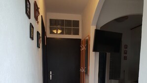 Uma área de refeições com mesa e cadeiras, uma porta escura e uma TV fixada na parede.