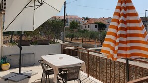 Um pátio externo com uma mesa e cadeiras, um guarda-sol branco e um guarda-sol listrado.