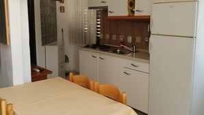 Cozinha compacta com mesa, cadeiras, geladeira, fogão e pia.