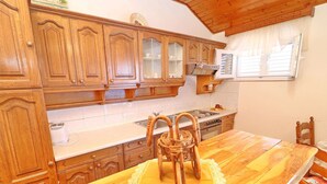 A kitchen with wooden cabinets, a stove, and a dining table with a woven basket. - Apartments Peselj-one Bedroom Apartment With Balcony and Sea View (Smokvica)