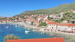 A coastal town with buildings along the waterfront, boats docked in the marina, and a hillside in the background. - Apartments Peselj-one Bedroom Apartment With Balcony and Sea View (Smokvica)