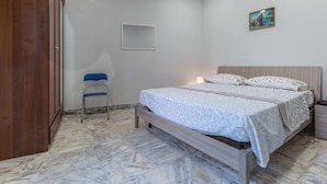 A bedroom with a bed, a wooden wardrobe, a chair, a nightstand, and a wall-mounted picture.