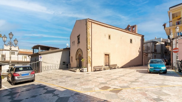 A building with a tiled courtyard, a parked car, and a street lamp.