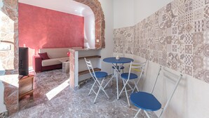 A compact room with a stone wall, a red accent wall, a patterned tile wall, a marble floor, a small table with chairs, and a sofa.