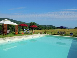 A swimming pool with lounge chairs and umbrellas, surrounded by a grassy field and hills. - Farmhouse Passignano Near Lake Trasimeno (Passignano sul Trasimeno)