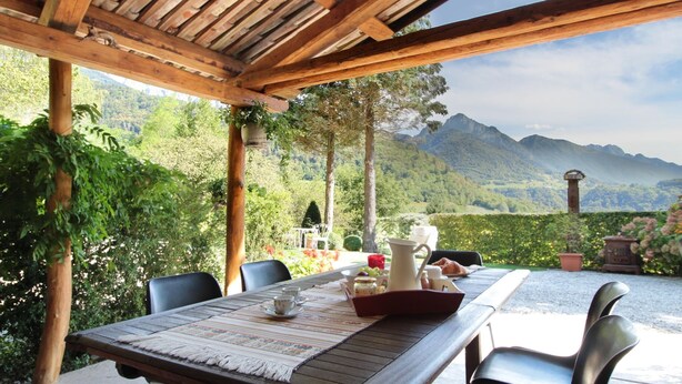 An outdoor dining area with a wooden pergola, a table set with a placemat, cups, a pitcher, and a basket of bread. - Holiday Home in Feltre With Garden BBQ (Pedavena)