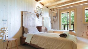 A wooden cabin bedroom with two beds, a small table, and a window with a view of greenery. - Holiday Home in Feltre With Garden BBQ (Pedavena)