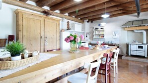 A rustic kitchen with wooden beams, a long wooden table, and a white stove. - Holiday Home in Feltre With Garden BBQ (Pedavena)
