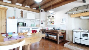 A rustic kitchen with wooden beams, a wooden table, and white cabinets. - Holiday Home in Feltre With Garden BBQ (Pedavena)