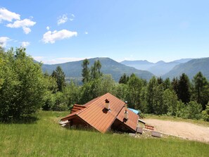 A house with a slanted roof in a grassy area with mountains in the background. - Alpine Getaway for Families (Lamon)