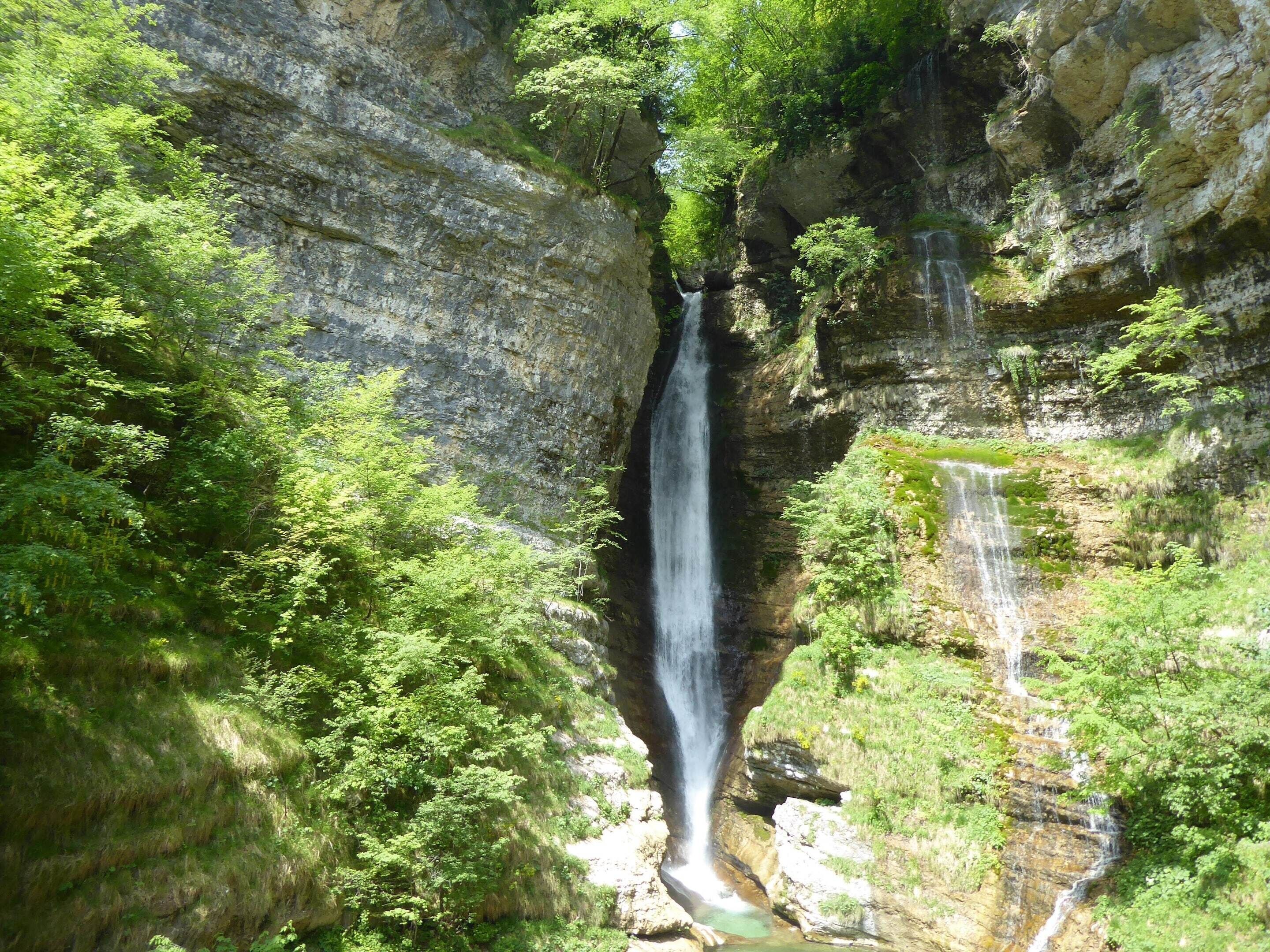 A waterfall cascading down a rocky cliff surrounded by lush greenery.