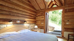 A wooden cabin bedroom with a bed, a nightstand, a lamp, and a stone wall. - Alpine Getaway for Families (Lamon)
