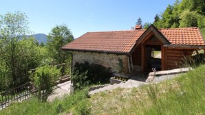A rustic cabin with a stone exterior and a red-tiled roof, surrounded by lush greenery and a clear sky. - Alpine Getaway for Families (Lamon)