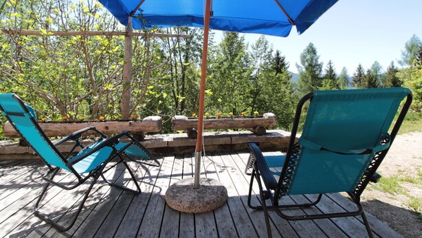 A wooden deck with two turquoise lounge chairs and a large blue umbrella. - Alpine Getaway for Families (Lamon)