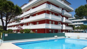 Un edificio de varios pisos con balcones, piscina y valla verde.