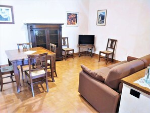 Un salon comprenant une table à manger en bois, des chaises, un canapé, un téléviseur et des tableaux encadrés accrochés au mur.