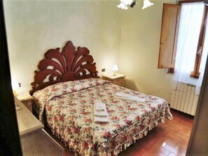 Une chambre à coucher avec une couvre-lit à motifs floraux, une tête de lit en bois, des tables de chevet avec des lampes et une fenêtre avec des rideaux.